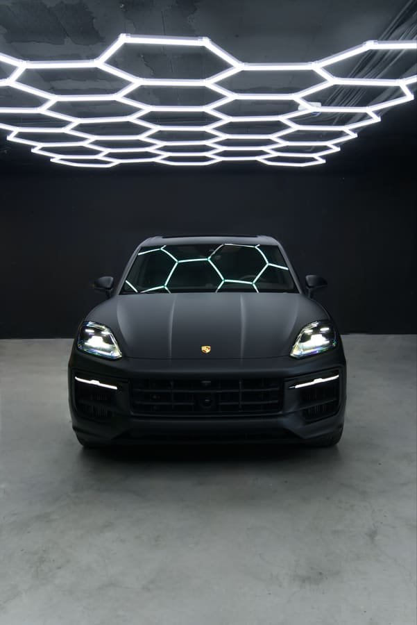 Porsche Cayenne con Car Wrap negro satinado, vista frontal bajo las luces hexagonales del estudio