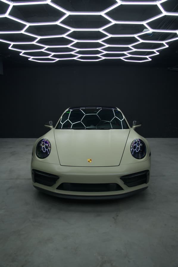 Porsche 911 Carrera GTS con Car Wrap arena satinado, vista frontal con las luces hexagonales reflejadas en el parabrisas