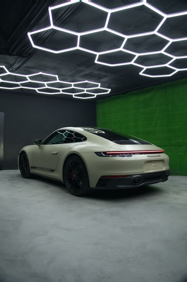 Porsche 911 Carrera GTS con Car Wrap arena satinado, tres cuartos trasero junto a la pared verde del estudio