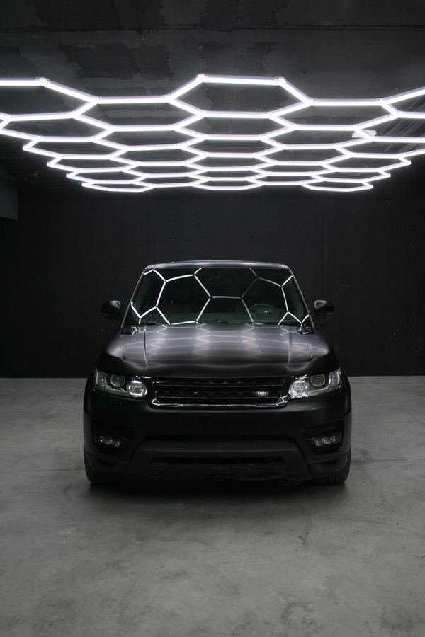 Range Rover Sport con Car Wrap negro satinado, vista frontal bajo las luces hexagonales del estudio